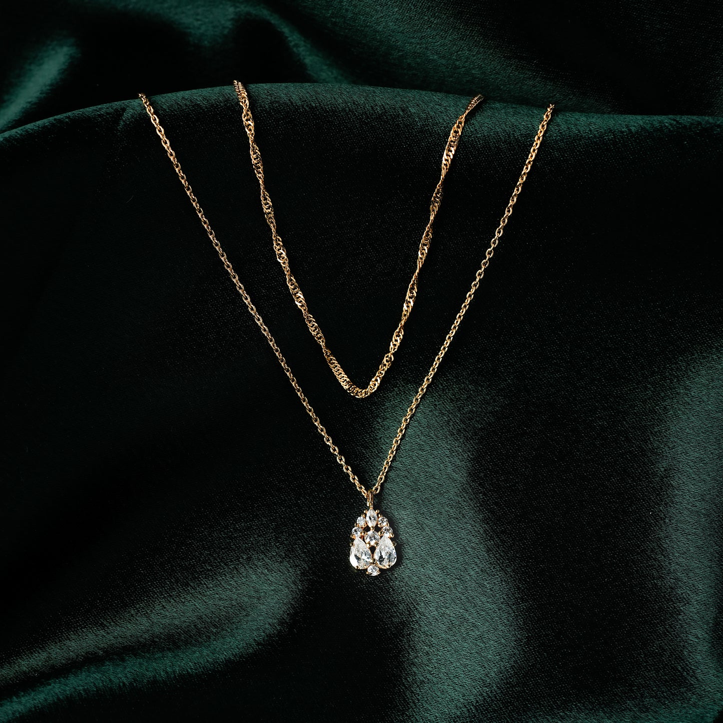 Layered gold necklace for women featuring a twisted chain and teardrop cubic zirconia pendant — elegant and dainty demi-fine jewellery on green satin backdrop