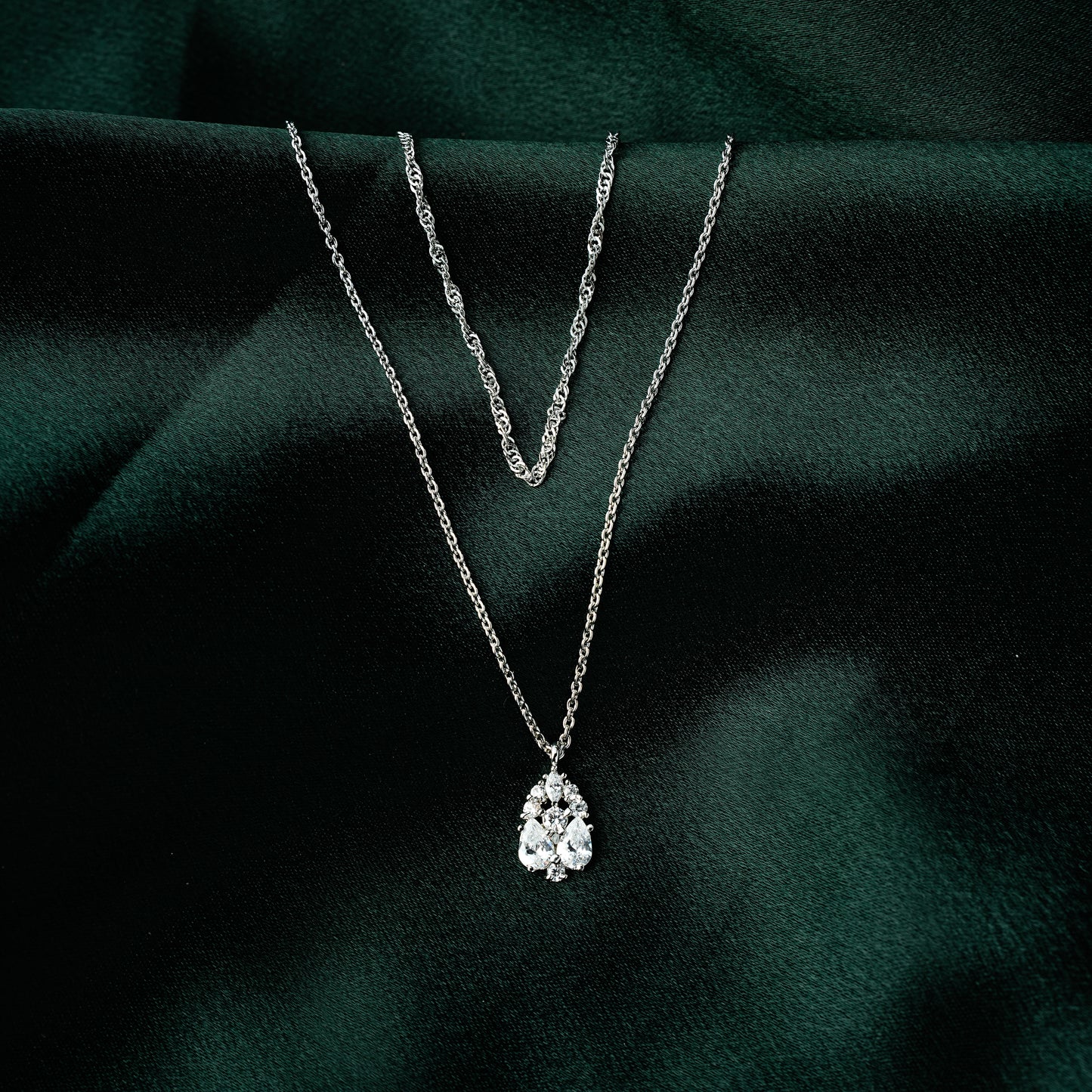 Layered gold necklace for women featuring a twisted chain and teardrop cubic zirconia pendant — elegant and dainty demi-fine jewellery on green satin backdrop