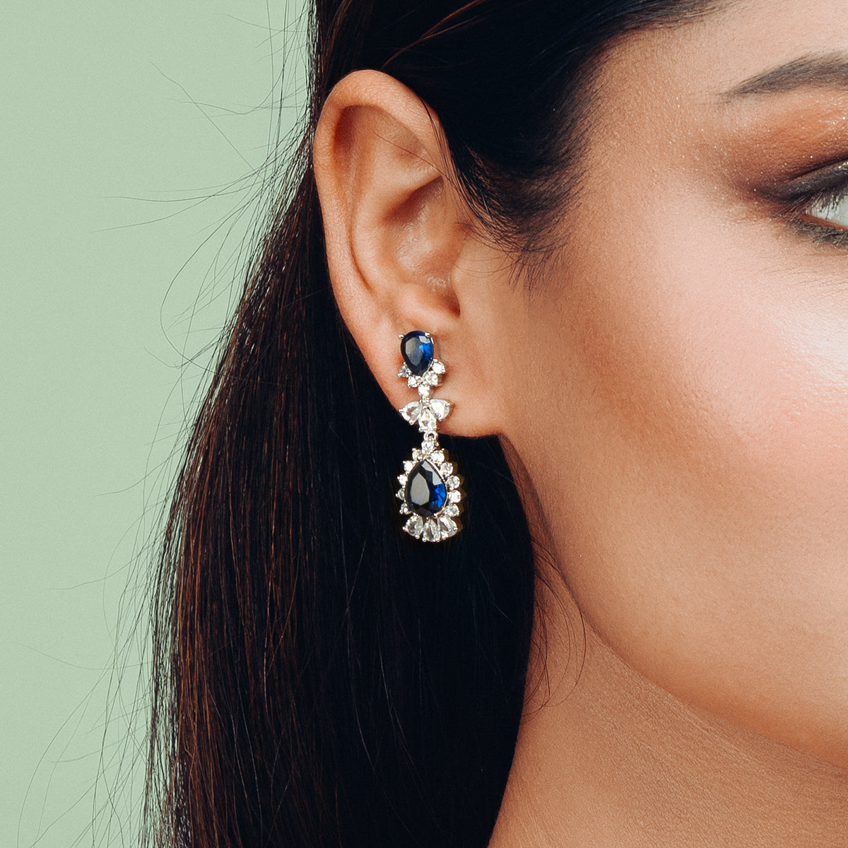 Model wearing Gulban’s Luxe Blue Sapphire Earrings, a regal pair of demi fine jewellery crafted with 18k gold plated finish and deep blue stones, featuring teardrop sapphire accents surrounded by sparkling zircons, perfect for elevated festive and evening looks