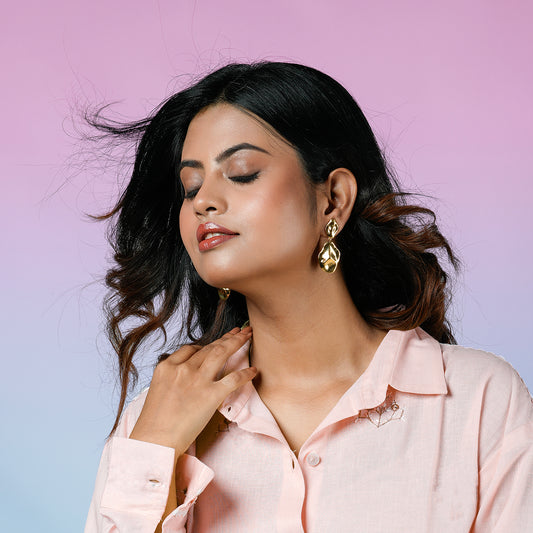 Elegant Sense Drop Earring in gold tone, worn by model with soft makeup and wavy hair, showcasing luxury statement jewellery by Gulban against a pastel pink and blue background for a sophisticated and fashionable look