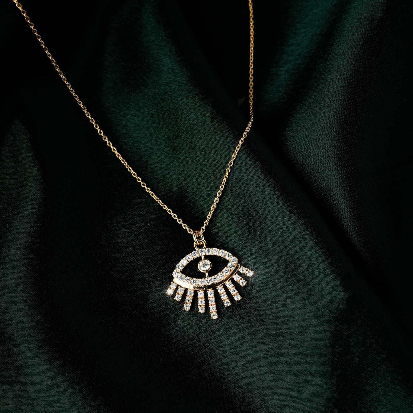 Gold eye pendant necklace for women with sparkling cubic zirconia stones in a minimalist modern design — demi-fine jewellery photographed on dark green satin
