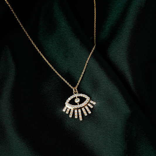 Gold eye pendant necklace for women with sparkling cubic zirconia stones in a minimalist modern design — demi-fine jewellery photographed on dark green satin