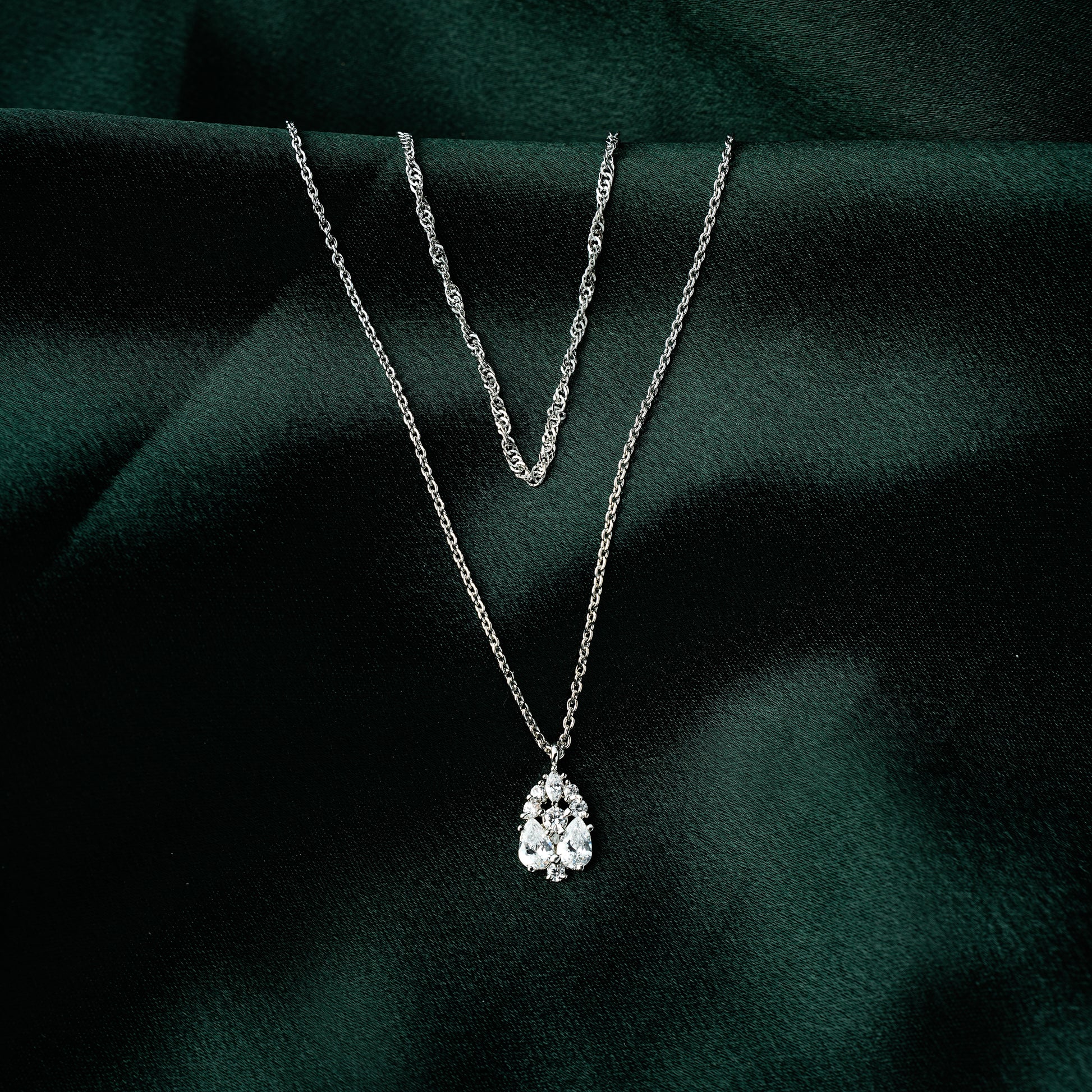 Layered gold necklace for women featuring a twisted chain and teardrop cubic zirconia pendant — elegant and dainty demi-fine jewellery on green satin backdrop